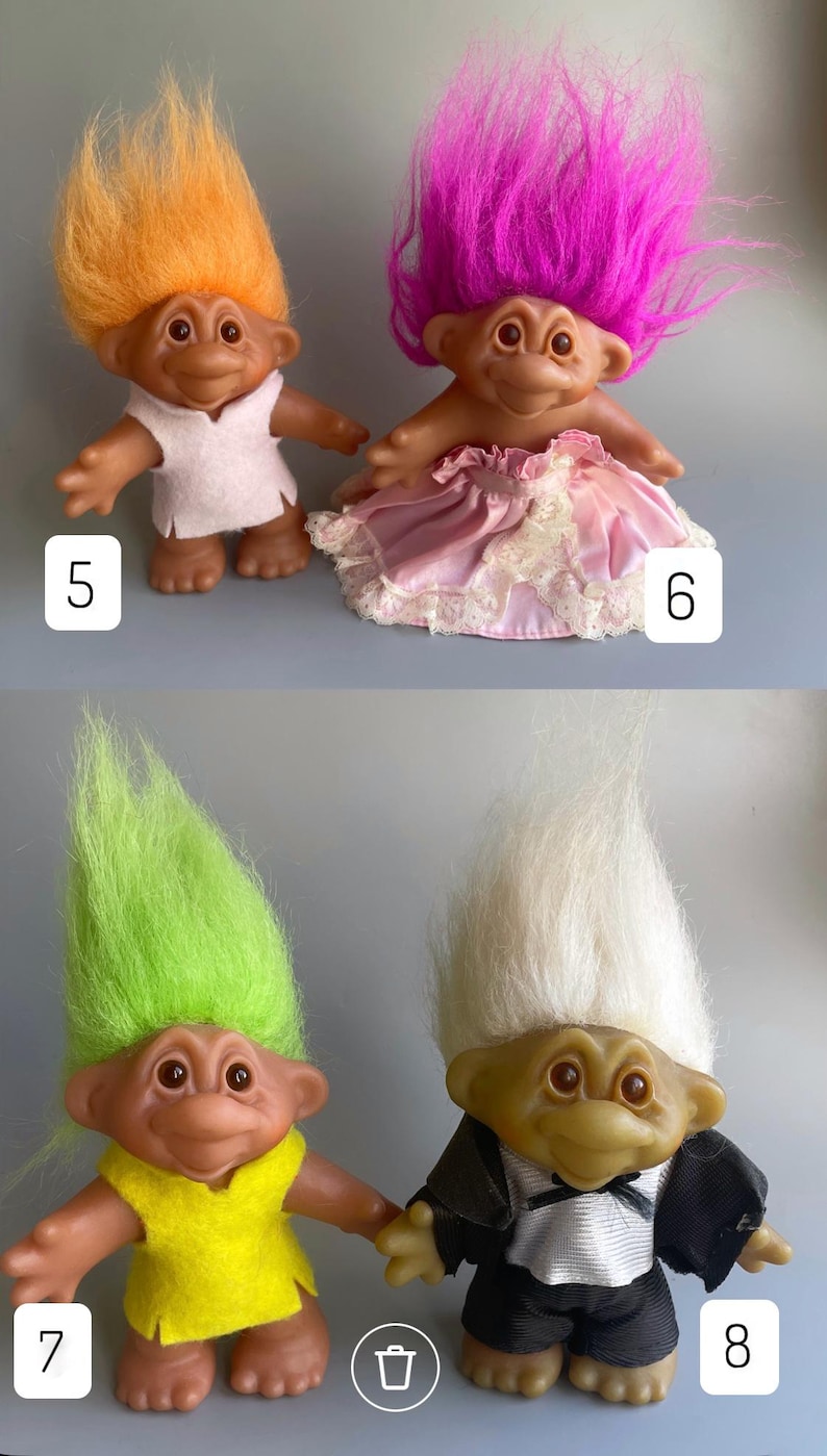 May include: Four troll dolls, two with pink and white dresses and two with yellow and black outfits. The dolls have different colored hair, including orange, pink, green, and white.