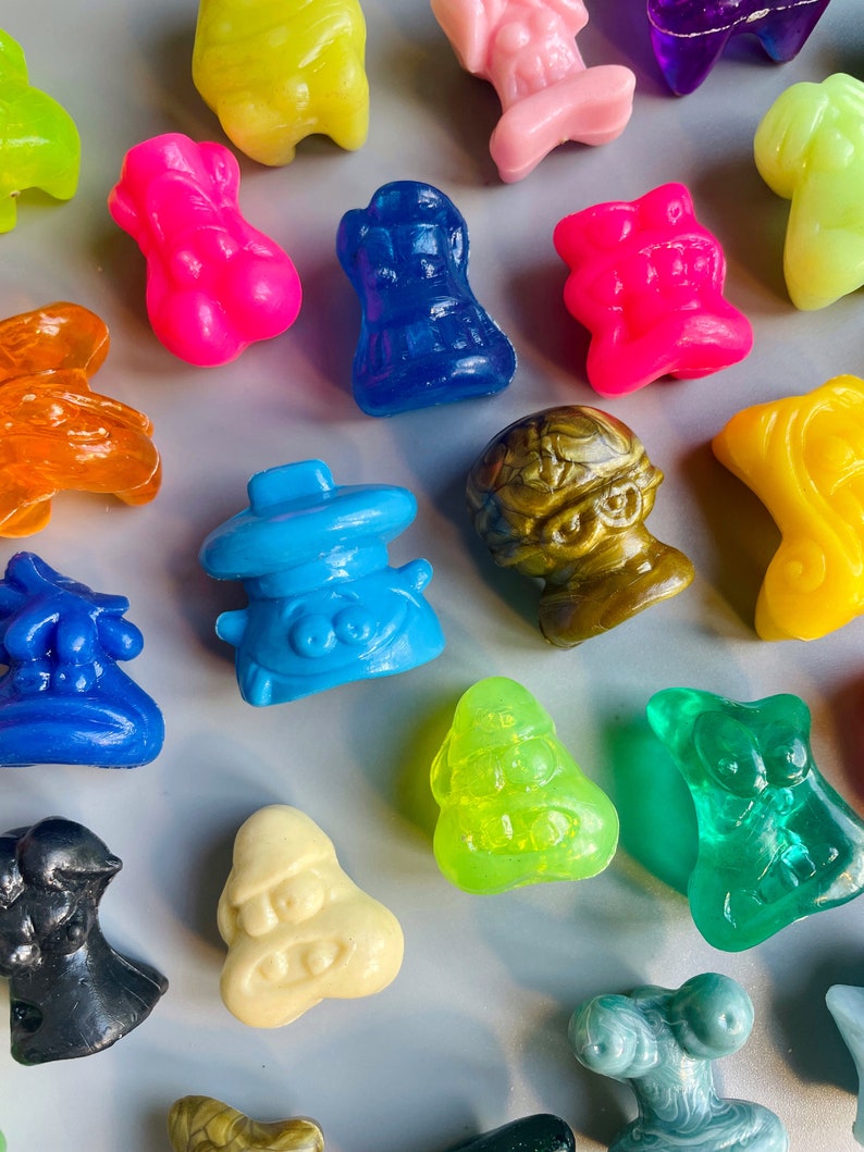 May include: A collection of colorful, small, plastic figurines. The figurines are in various shapes and designs, including a blue alien, a green monster, a yellow creature, and a pink character. The figurines are all about 2 inches tall.