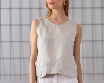 May include: A woman wearing a light gray sleeveless linen top with a v-neck and white pants.