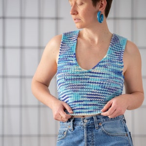 Op de afbeelding: Een vrouw draagt een blauw en wit gestreept gebreid tanktop met een v-hals en een blauwe jeans.