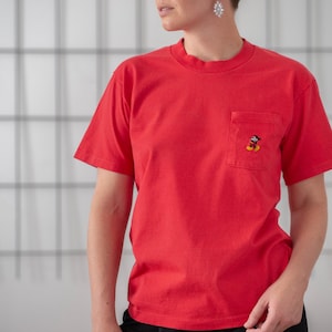 May include: A red short-sleeved t-shirt with a small embroidered Mickey Mouse image on the left chest pocket.