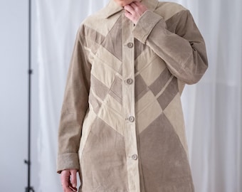 May include: A tan suede jacket with a geometric design. The jacket features a collared neckline, long sleeves, and a button-down front. The jacket is worn with blue jeans.