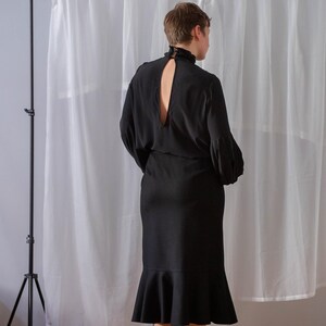 Pode incluir: Um vestido preto com gola alta e um decote nas costas em forma de buraco de fechadura. O vestido tem um corpete justo e uma saia rodada.