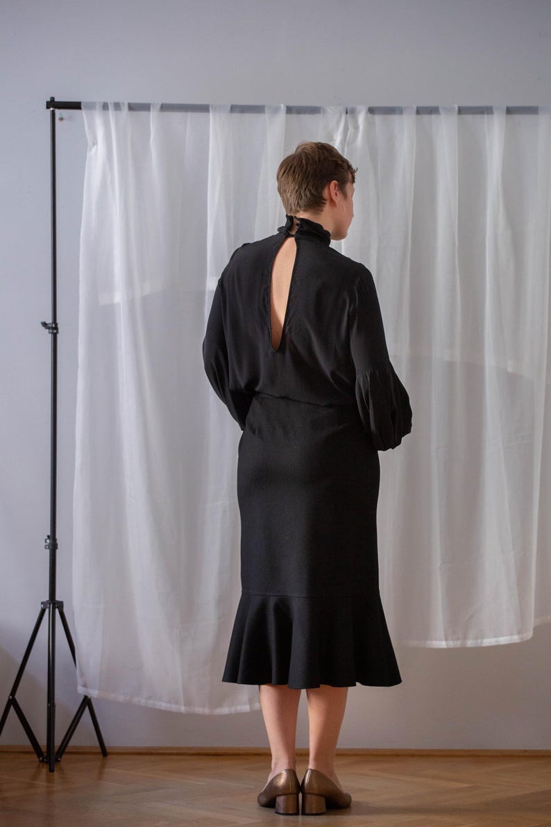 Pode incluir: Um vestido preto com gola alta e um decote nas costas em forma de buraco de fechadura. O vestido tem um corpete justo e uma saia rodada.