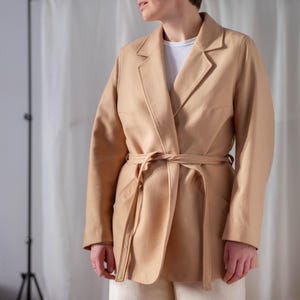 May include: A tan wrap coat with a self-tie belt. The coat has a long sleeve and a relaxed fit.
