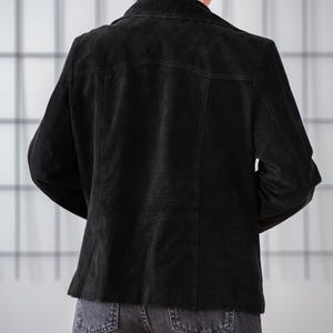 May include: A black suede jacket with a classic design. The jacket has a collar, long sleeves, and a button closure. The jacket is shown from the back.