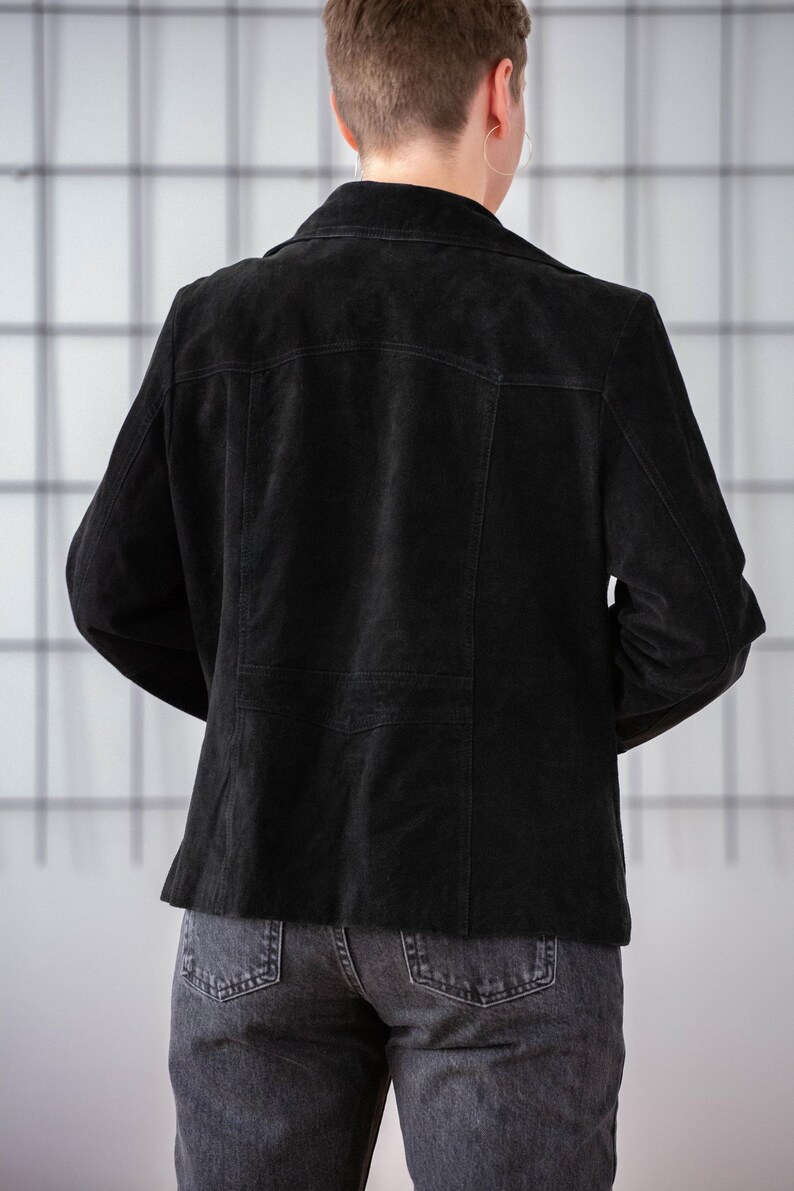 May include: A black suede jacket with a classic design. The jacket has a collar, long sleeves, and a button closure. The jacket is shown from the back.