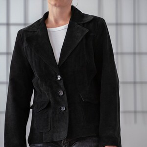 May include: A black suede jacket with a button fastening and a single pocket on the left side.