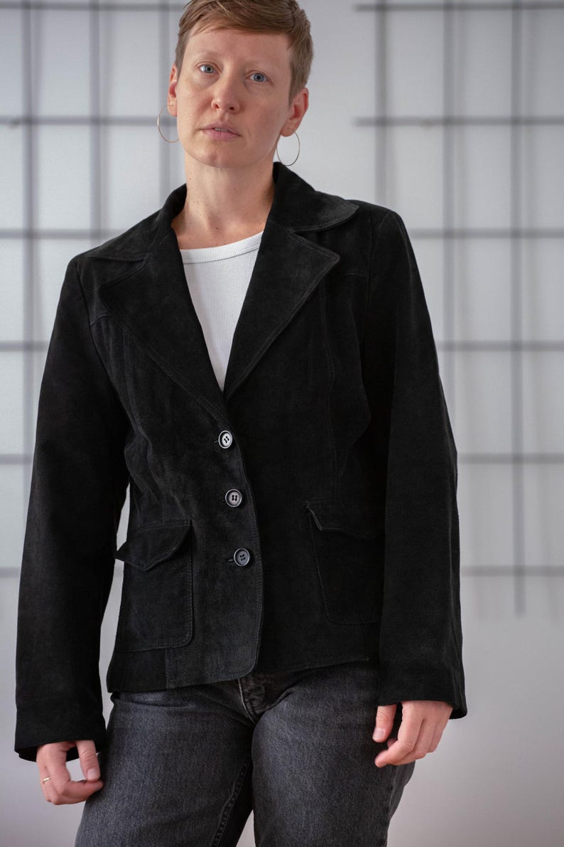 May include: A black suede jacket with a button fastening and a single pocket on the left side.