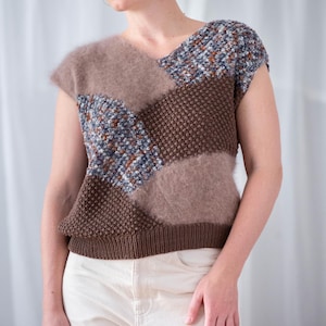 Peut inclure: Un haut en tricot patchwork dans les tons de marron, beige et bleu. Le haut sans manches présente un motif en tricot texturé et une matière douce et duveteuse. Le haut est porté avec un pantalon crème.