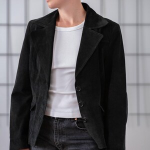 May include: A black suede blazer with a single button fastening. The blazer has a notched collar and a relaxed fit.