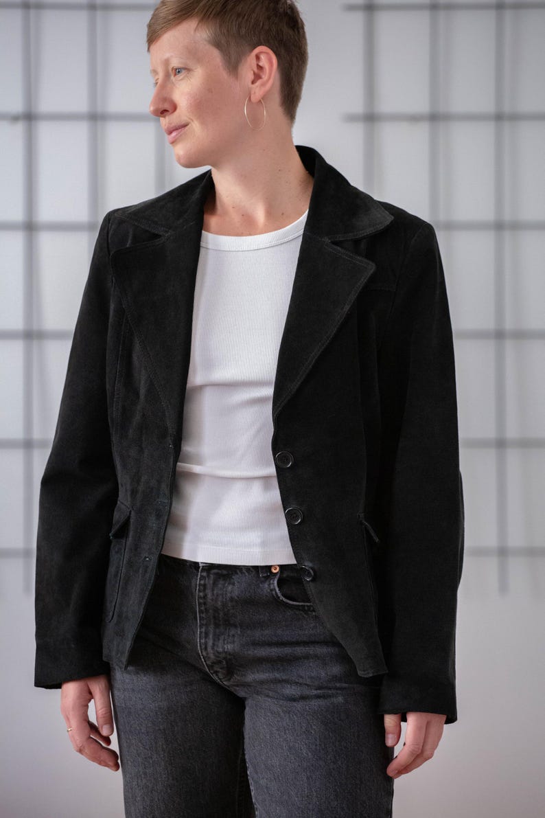 May include: A black suede blazer with a single button fastening. The blazer has a notched collar and a relaxed fit.