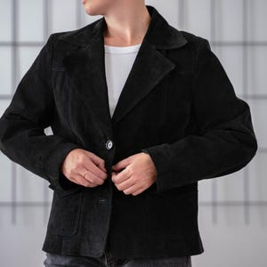 May include: A black suede jacket with a single button fastening and a pocket on the left side.