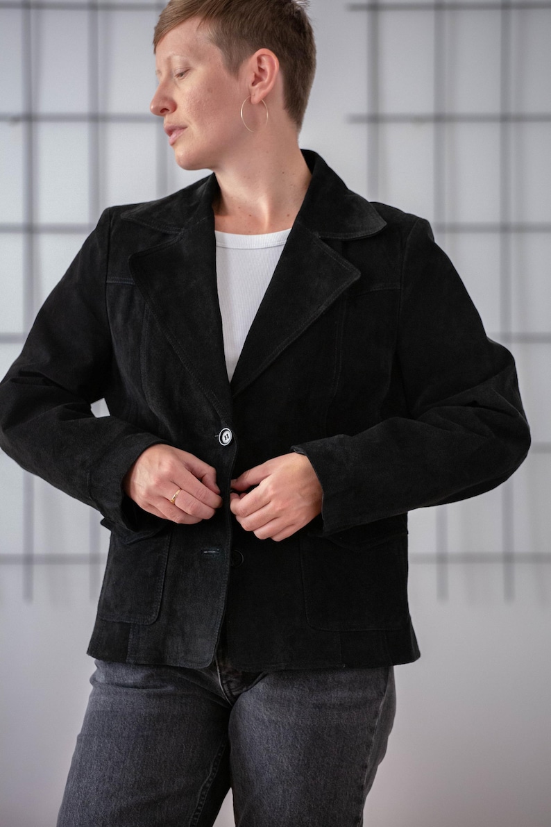 May include: A black suede jacket with a single button fastening and a pocket on the left side.