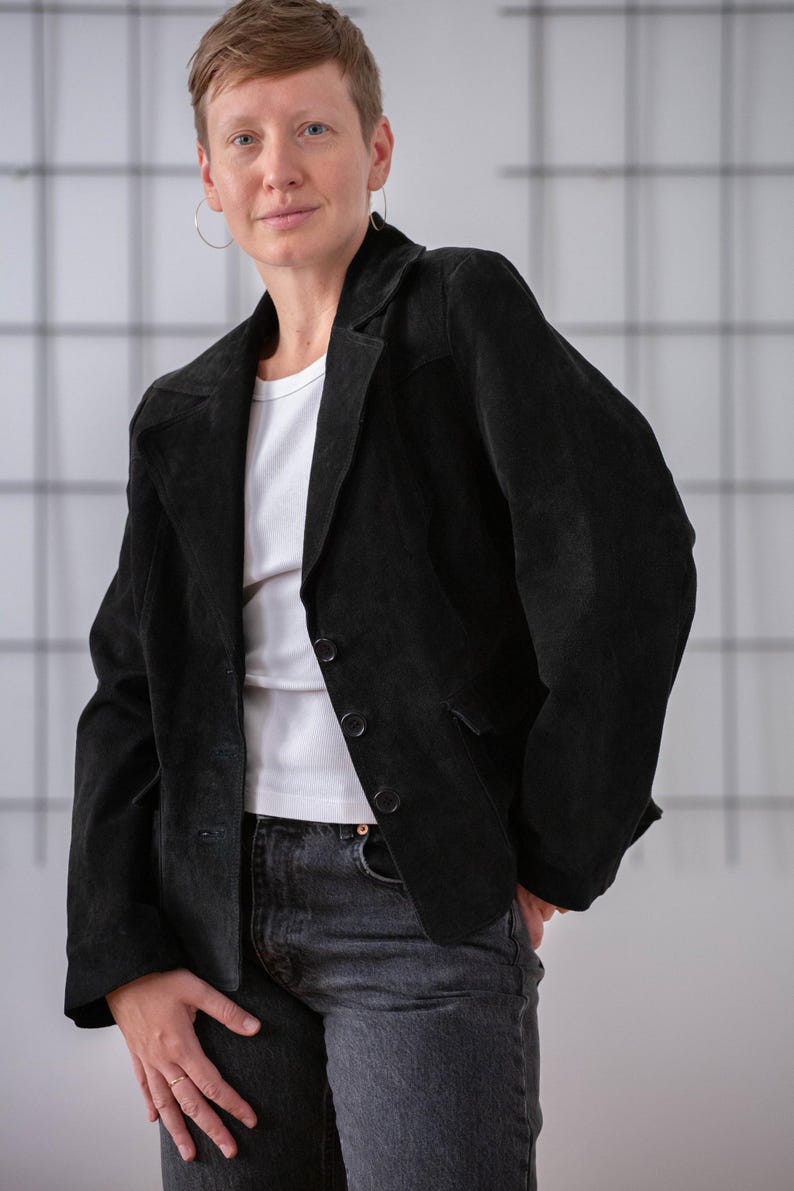 May include: A person wearing a black suede blazer with a white t-shirt and dark wash jeans.