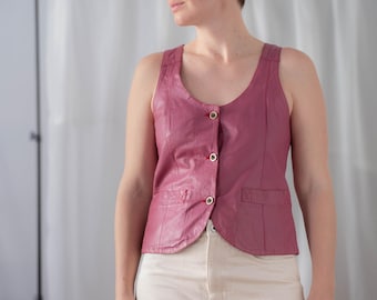 May include: A woman wearing a pink leather vest with gold buttons and white pants.