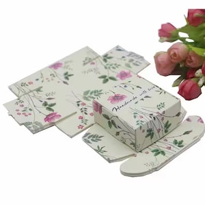 May include: A white gift box with a floral pattern and the text "Handmade with love". The box is made of cardboard and has a hinged lid. The box is decorated with pink flowers and green leaves.