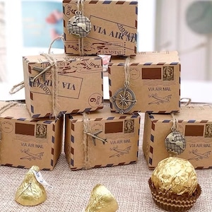 May include: Six small brown cardboard boxes with a vintage airmail design. Each box has a different charm attached to it, including a compass, a globe, and an airplane. The boxes are tied with twine and have the words "VIA AIR MAIL" printed on them.