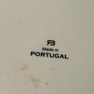 May include: Close-up of a white ceramic surface with the text "Made in PORTUGAL" in black. The image also features a stylized "B" logo. The surface has minor imperfections.