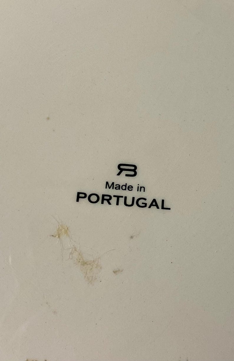 May include: Close-up of a white ceramic surface with the text "Made in PORTUGAL" in black. The image also features a stylized "B" logo. The surface has minor imperfections.