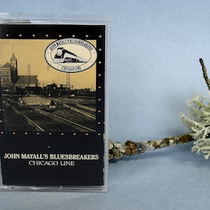 May include: A vintage cassette tape for John Mayall's Bluesbreakers Chicago Line album. The cassette case is clear, with a black and tan cover featuring a train and a railway scene. The album title is printed in white.