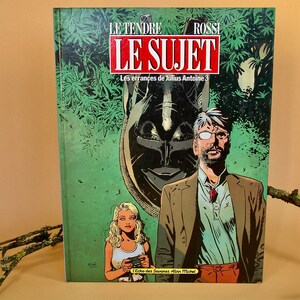 May include: A comic book titled "LE SUJET" with the text "Les errances de Julius Antoine 3". The cover features illustrations of a man, a woman, and a tribal mask against a green background. The book's title is in red and white.