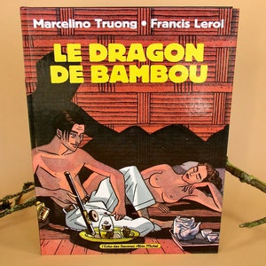 Peut inclure: Couverture de bande dessinée "LE DRAGON DE BAMBOU" avec des illustrations de deux personnes dans un sauna. Le titre est en jaune. Les noms des auteurs, Marcelino Truong et Francis Leroi, sont en haut. La scène montre un homme avec une pipe.