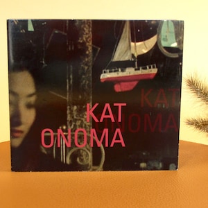 May include: A black and white CD cover with a pink and white sailboat in the background. The text "KAT ONOMA" is printed in pink on the front of the CD cover.