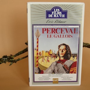 May include: A VHS tape case with a white background and gold accents. The title "LES FILMS DE MA VIE" is printed in blue at the top. The title of the film "PERCEVAL LE GALLOIS" is printed in blue and white. The film is directed by Eric Rohmer. The case features a colorful illustration of a knight in armor.
