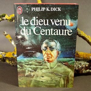 Peut inclure: Une couverture de livre de poche avec une illustration colorée d'un homme sur un fond étoilé. Le titre du livre est "le dieu venu du Centaure" de Philip K. Dick.