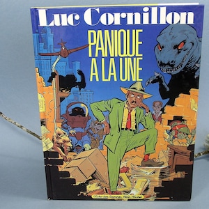 May include: A comic book cover with the title "Panique A La Une" by Luc Cornillon. The cover features a man in a green suit, a dinosaur, and other cartoon characters against a blue cityscape background.