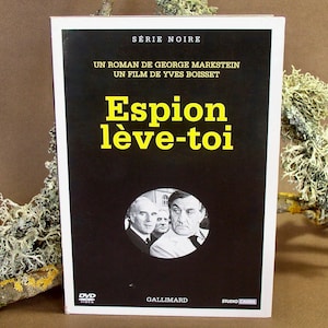 Peut inclure: DVD du film français "Espion lève-toi" avec une couverture noire et une bordure blanche. Le titre est en jaune, avec une image en noir et blanc de trois hommes dans un cercle. Le DVD est de Gallimard et Studio Canal.