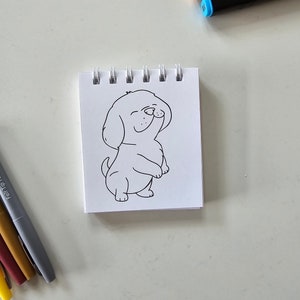 May include: A black and white line drawing of a dog on a white sheet of paper in a spiral bound notebook.