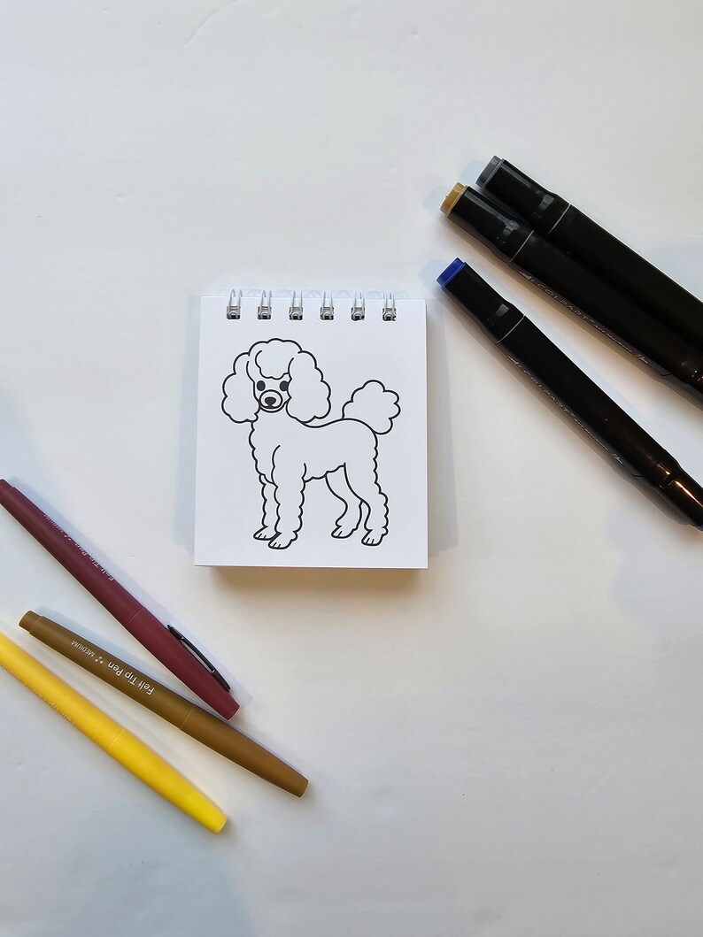 May include: A white, line-drawn illustration of a poodle on a small, white notepad. The notepad is surrounded by three markers: one brown, one yellow, and one black.