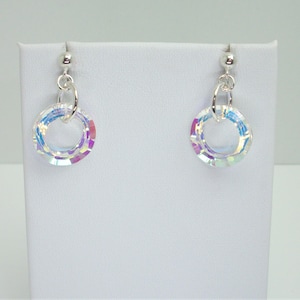 May include: A white ceramic mug with a black handle and the text "But First, Coffee" in a bold, black font. The mug is set against a blurred background, suggesting a cozy setting.