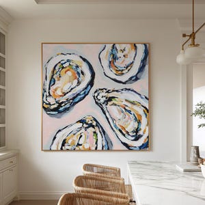 May include: Large square abstract painting of four oyster shells in shades of blue, white, orange, and yellow on a pink background. The painting is in a gold frame and hangs above a marble countertop.