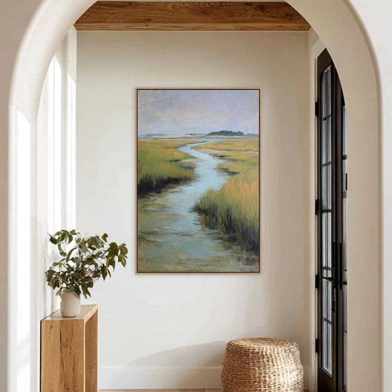 May include: A framed landscape painting depicts a marsh scene with a winding waterway. The artwork features a palette of greens, blues, and yellows, with a muted sky. The painting is displayed in a bright hallway, adding a touch of nature to the interior.