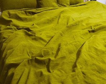 Puede incluir: Una funda nórdica de lino verde con fundas de almohada a juego. La funda nórdica está arrugada y tiene una textura suave y natural.