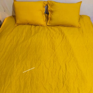 May include: A yellow bedspread with two yellow pillowcases. The bedspread is wrinkled and has a subtle sheen.