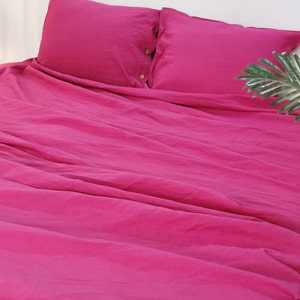 May include: A deep pink linen duvet cover with two matching pillowcases. The duvet cover has a button closure and the pillowcases have a simple design.