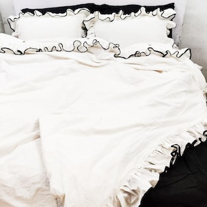 Puede incluir: Juego de cama blanco con ribete de volantes negros. El juego incluye una funda nórdica y dos fundas de almohada.