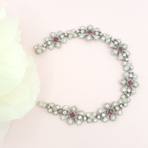 May include: A silver bracelet with a delicate floral design and red gemstone accents.
