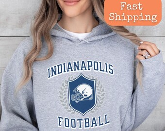 Könnte beinhalten: Ein grauer Kapuzenpullover mit dem Text "Indianapolis Football" und einer Grafik eines blauen und weißen Footballhelms. Der Text ist in weißer Umrandung mit blauer Füllung.