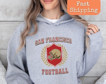 May include: A grey hooded sweatshirt with the text "San Francisco Football" and a red shield with a gold football helmet graphic.