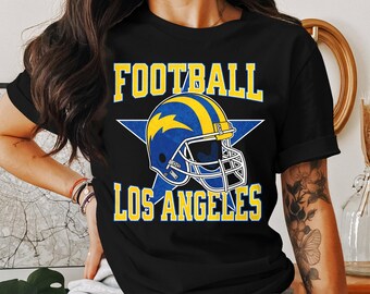 Op de afbeelding: Zwart T-shirt met een blauwe en gele voetbalhelm afbeelding en de tekst "FOOTBALL LOS ANGELES".