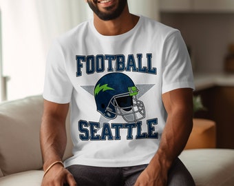 Op de afbeelding: Wit T-shirt met een blauwe en groene voetbalhelm afbeelding en de tekst "FOOTBALL SEATTLE".