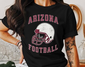 Op de afbeelding: Zwart T-shirt met een maroon grafische afbeelding van een voetbalhelm en de tekst "Arizona Football".