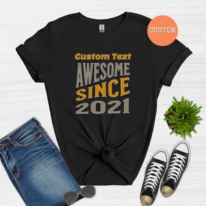 Peut inclure: T-shirt noir avec le texte "Custom Text Awesome Since 2021" en lettres orange et grises.
