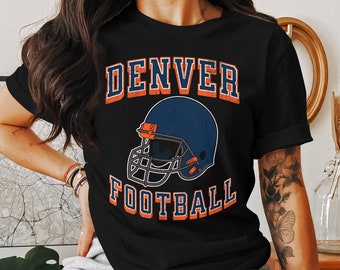 May include: Black t-shirt with a vintage-style graphic of a football helmet and the text "DENVER FOOTBALL" in orange and blue.