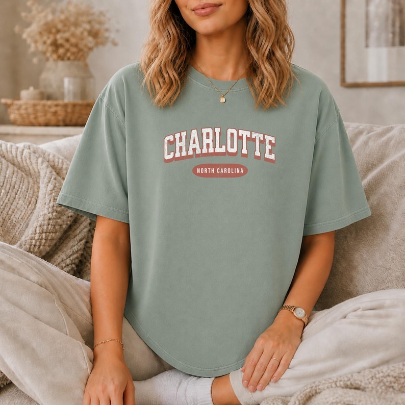 Sage green t-shirt with "CHARLOTTE NORTH CAROLINA" text in red and white.